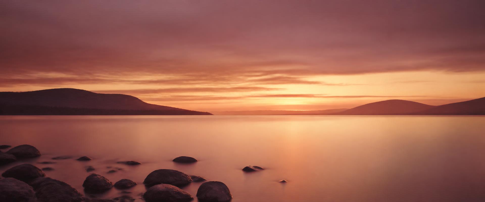 A calm shoreline at golden hour with smooth stones and still water